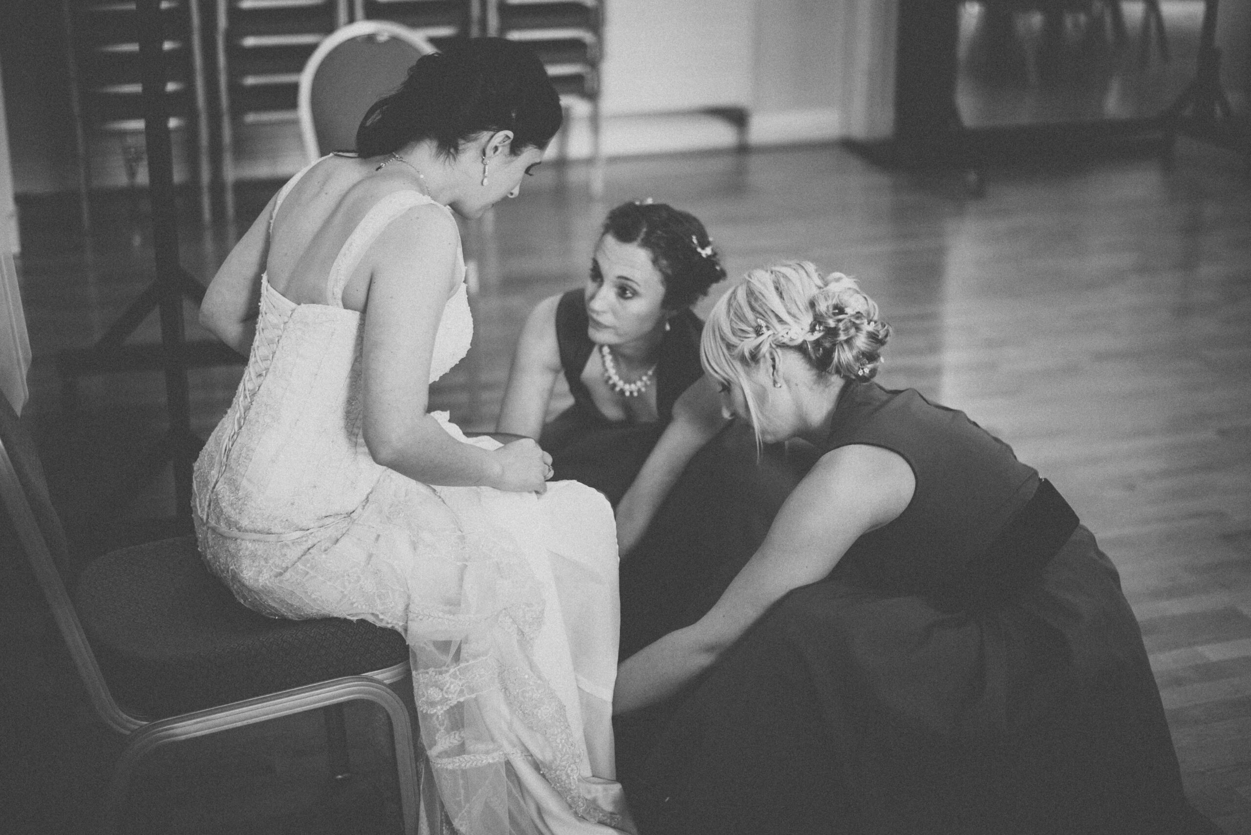 Bridebook.co.uk bridesmaids putting bride shoe on