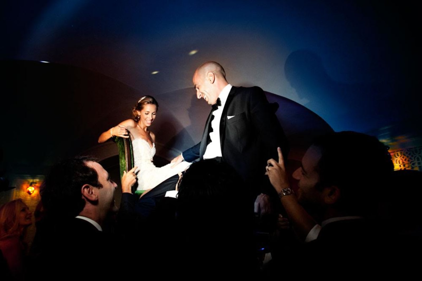 bridebook.co.uk-smashing-the-glass- couple on chairs being lifted up