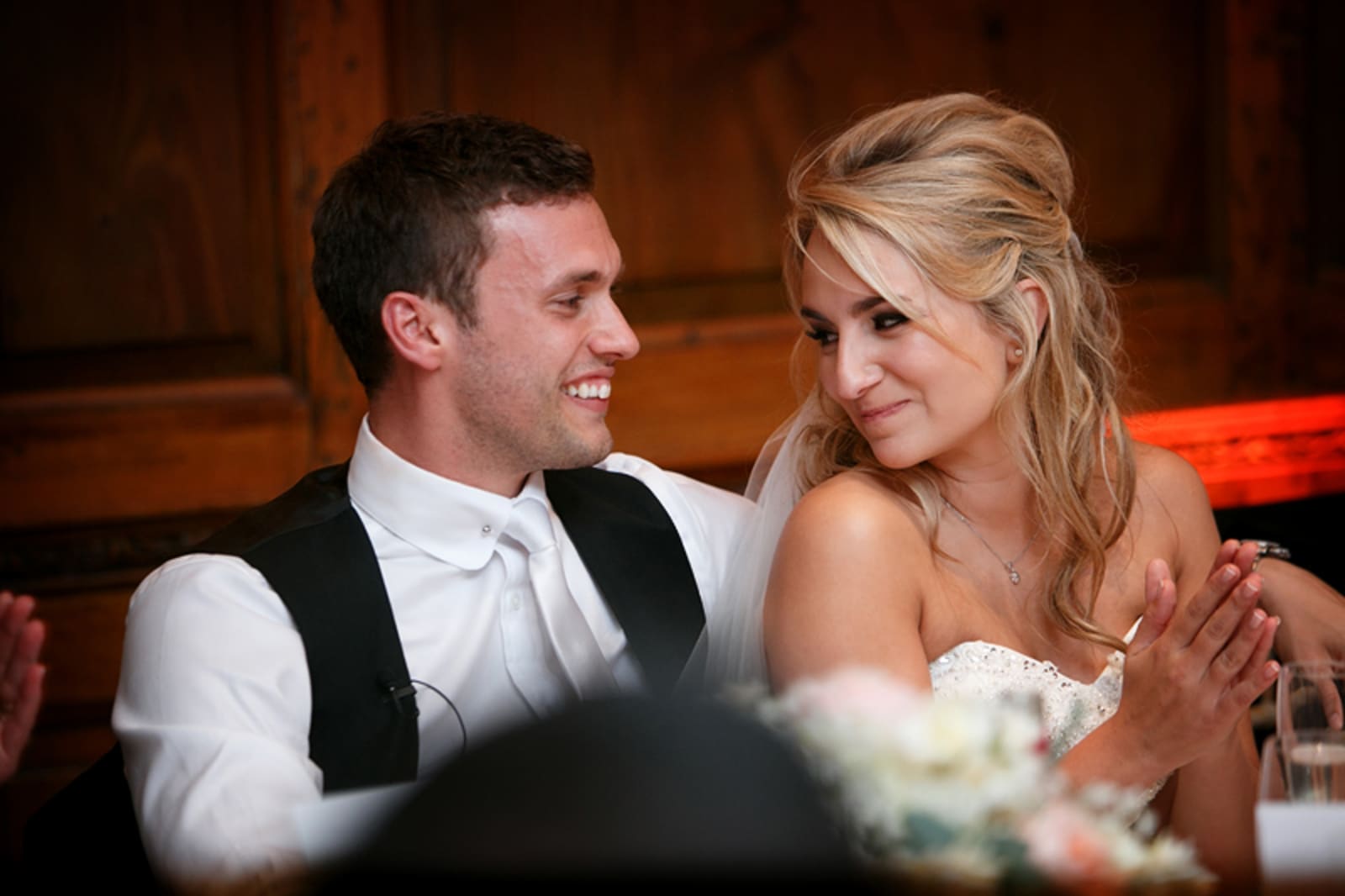 Bridebook.co.uk- bride and groom listening to speeches and smiling