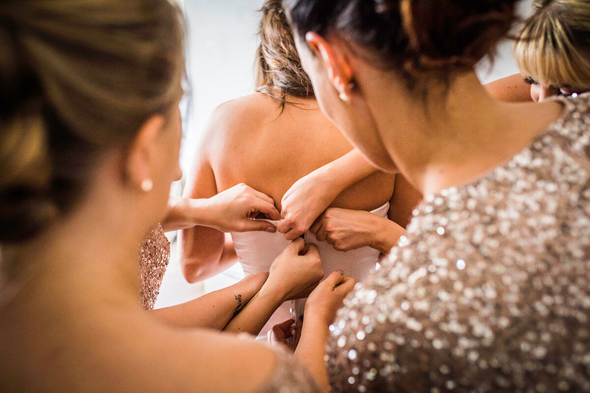 bridesmaids help close the bride's dress