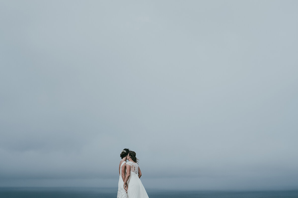 two brides kiss under cloudy skies