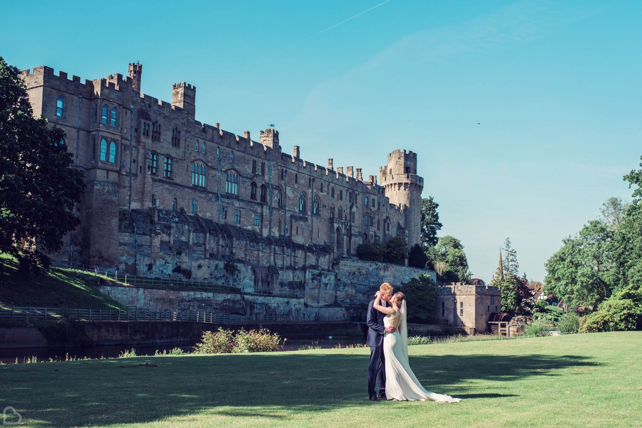 a couple kisses outside of warwick castle on a sunny day